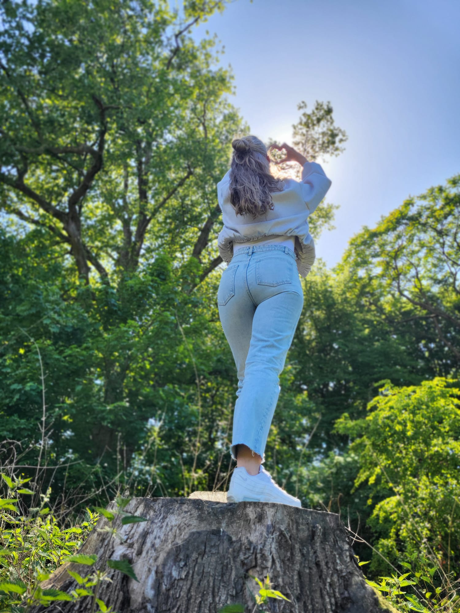 Karla staat in het bos, kijkt omhoog en maakt een hartje met haar handen
